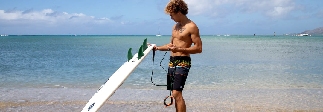 Surfer standing on Hawaii beach inspecting surfboard