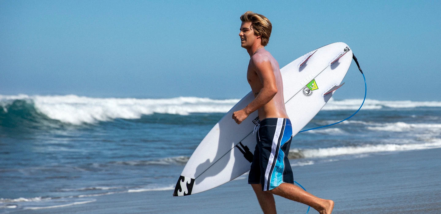 Man running on a beach with a surfboard under his arm.