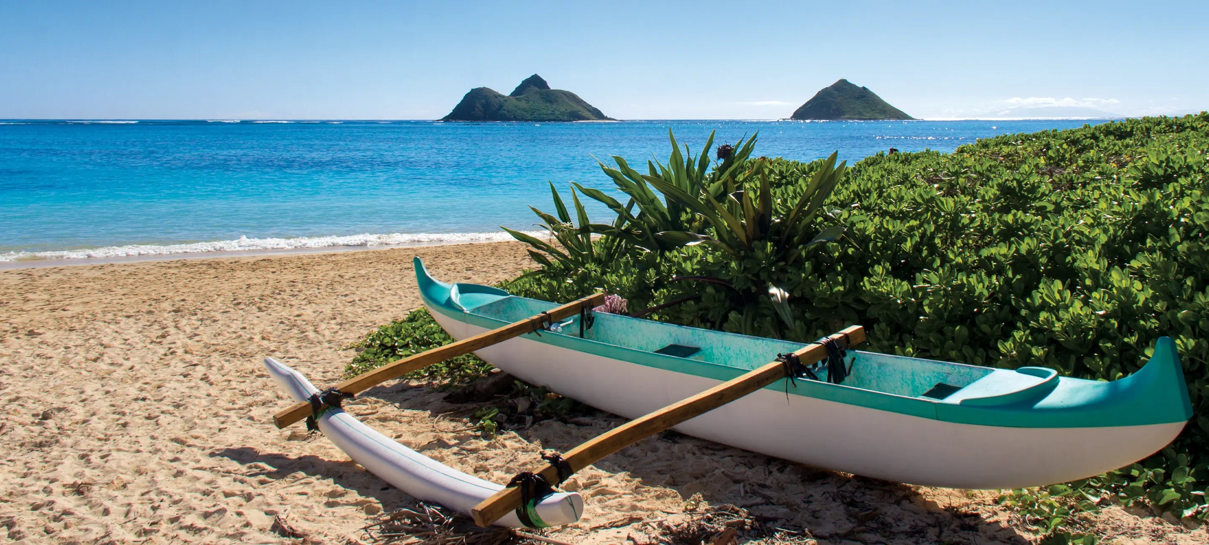 An outrigger canoe sits on Lanikai Beach with the Mokulua Islands in the background