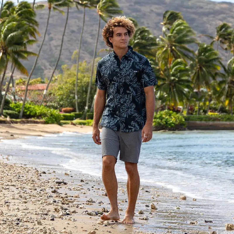 A man walks along the beach in HIC's Jocko aloha shirt and Porter Hybrid shorts